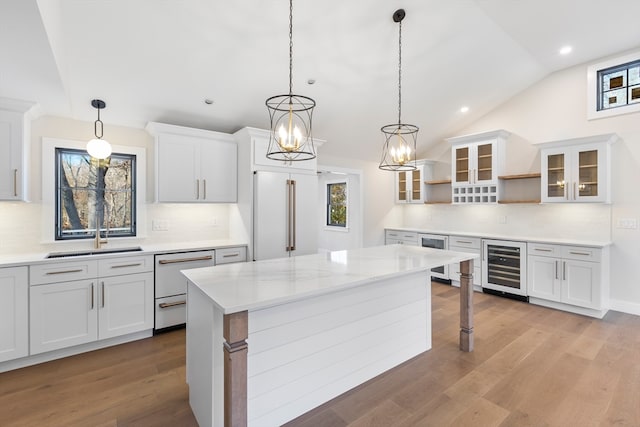 kitchen with light stone counters, sink, decorative light fixtures, white cabinetry, and lofted ceiling