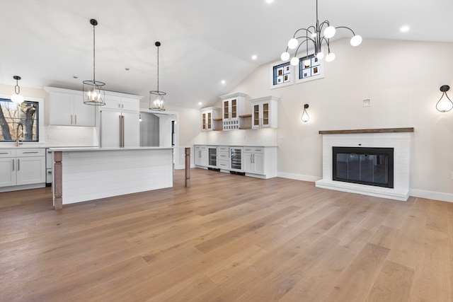 unfurnished living room featuring a brick fireplace, lofted ceiling, beverage cooler, and light hardwood / wood-style flooring