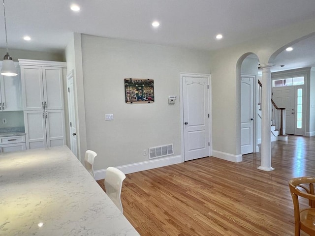 141 Pearl St Unit 141, Newton, MA 02458 - kitchen featuring arched walkways, ornate columns, light wood-type flooring, white cabinetry, and pendant lighting