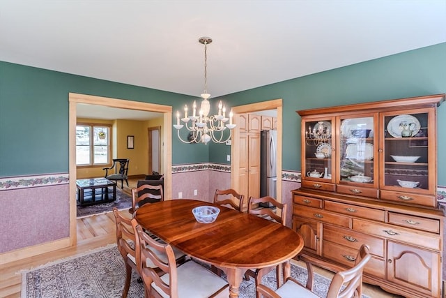 dining area with an inviting chandelier, wainscoting, and light wood-type flooring