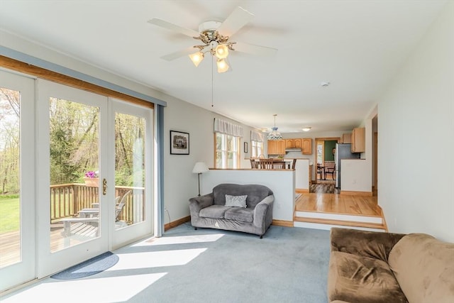 living area featuring a ceiling fan, baseboards, and light carpet