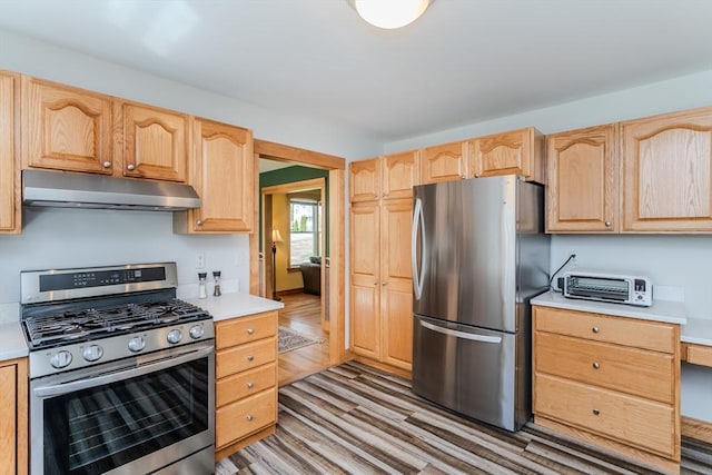 kitchen with light countertops, under cabinet range hood, light brown cabinets, stainless steel appliances, and light wood-style flooring