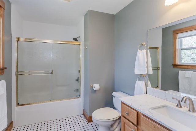 bathroom with vanity, baseboards, toilet, and shower / bath combination with glass door