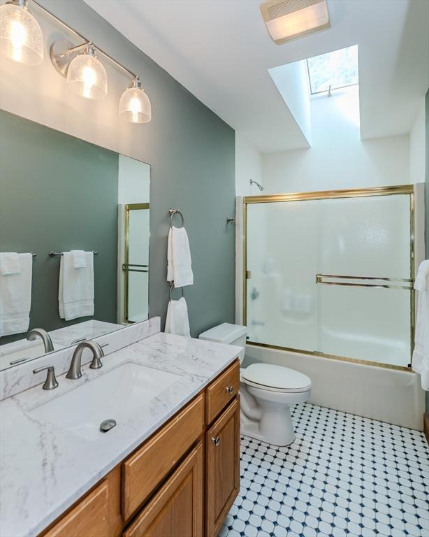 full bath featuring shower / bath combination with glass door, a skylight, toilet, and vanity