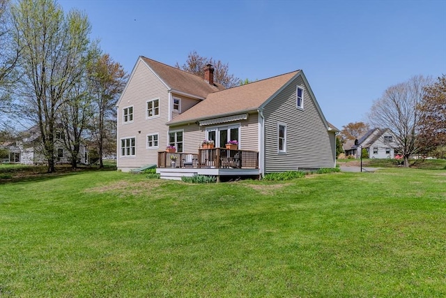 rear view of house with a chimney, a lawn, and a deck