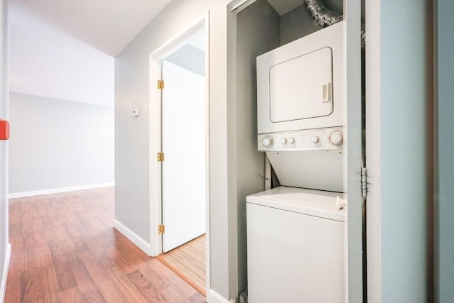 laundry area featuring stacked washer and clothes dryer, wood finished floors, and baseboards