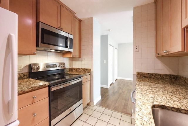 kitchen featuring stainless steel appliances, backsplash, light stone countertops, baseboards, and light tile patterned flooring