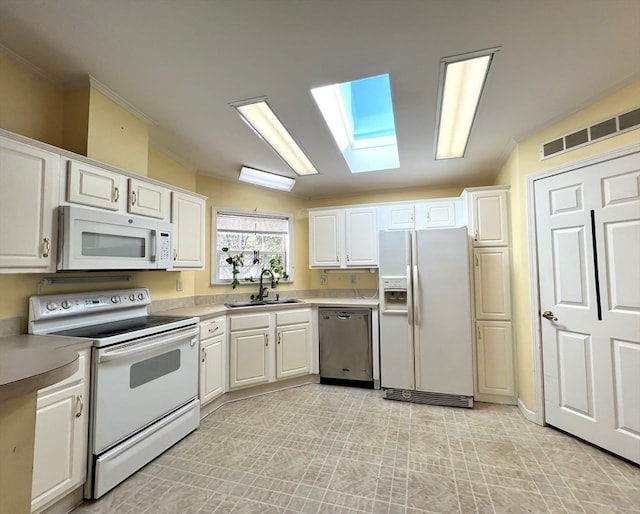 kitchen featuring vaulted ceiling with skylight, sink, white cabinetry, and white appliances