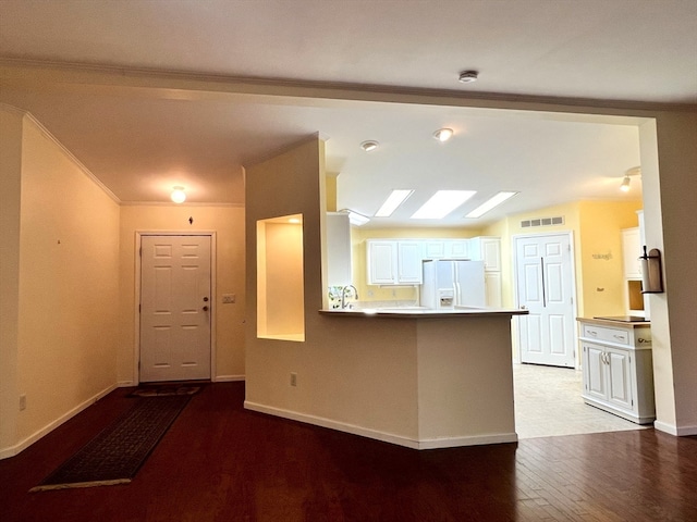 kitchen featuring white refrigerator with ice dispenser, kitchen peninsula, hardwood / wood-style floors, vaulted ceiling, and white cabinets