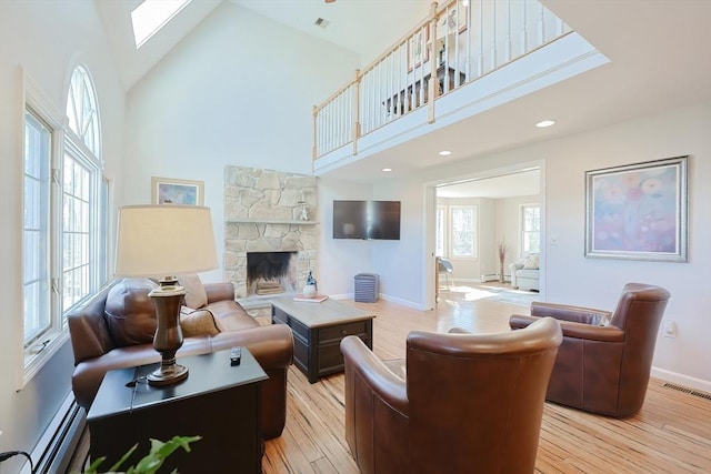 living area featuring visible vents, baseboard heating, light wood-style flooring, a skylight, and high vaulted ceiling