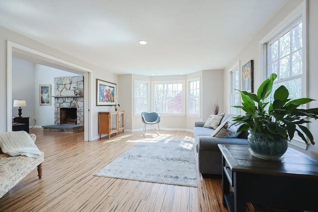 living room with a stone fireplace, wood finished floors, baseboards, and a healthy amount of sunlight