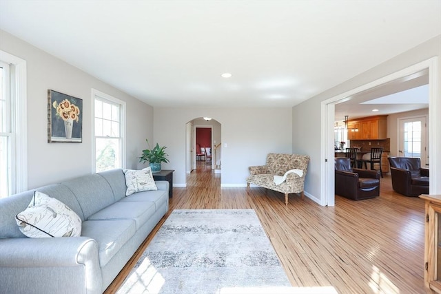 living area featuring recessed lighting, baseboards, arched walkways, and light wood-style flooring