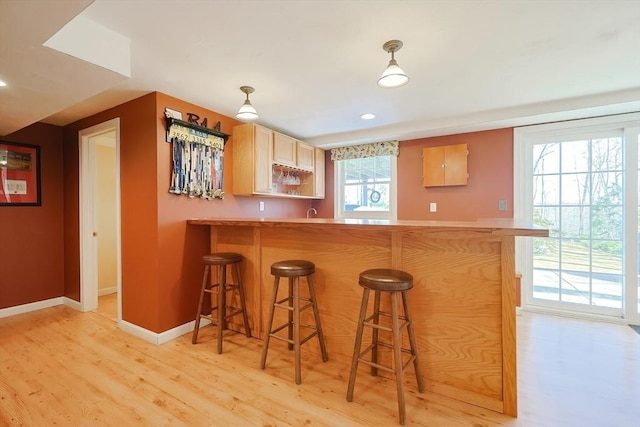 kitchen featuring light wood-style flooring, a peninsula, a breakfast bar area, and baseboards