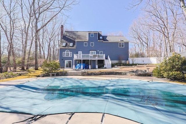 rear view of property with stairway, fence, a covered pool, a chimney, and a deck