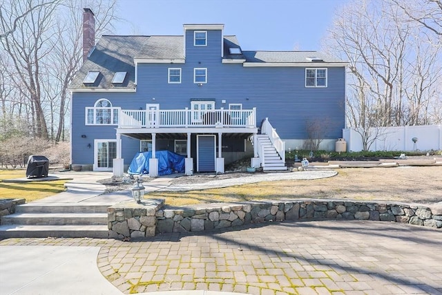 rear view of house featuring fence, stairway, a chimney, a deck, and a patio area