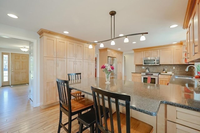 kitchen with light brown cabinets, a sink, stainless steel appliances, a peninsula, and decorative backsplash