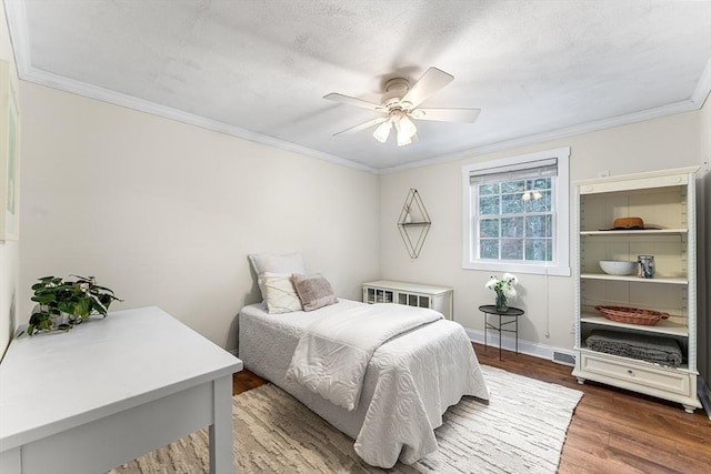 bedroom featuring ceiling fan, baseboards, ornamental molding, wood finished floors, and a textured ceiling