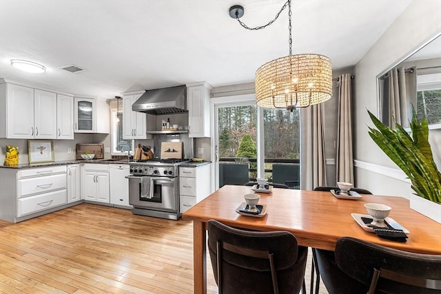 kitchen with light wood-style flooring, high end stainless steel range oven, white cabinetry, and wall chimney range hood