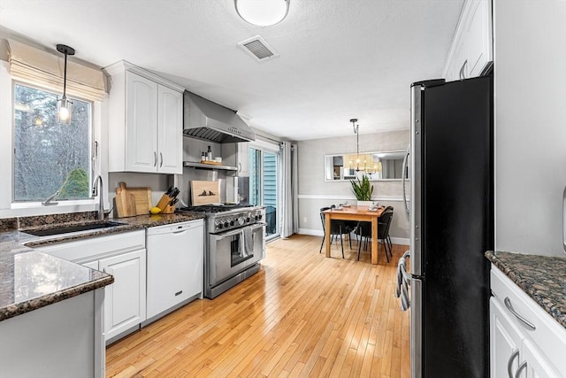 kitchen featuring wall chimney range hood, white cabinets, appliances with stainless steel finishes, and a sink