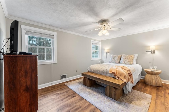 bedroom with multiple windows, wood finished floors, visible vents, and ornamental molding