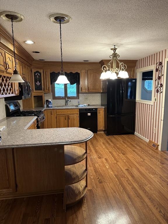 55 Alexander Ave, Dracut, MA 01826 - kitchen with black appliances, a textured ceiling, a peninsula, light countertops, and pendant lighting