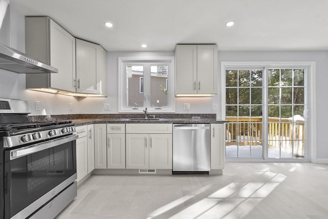 kitchen with recessed lighting, appliances with stainless steel finishes, white cabinets, a sink, and wall chimney range hood