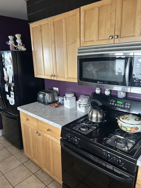 kitchen featuring light stone counters, light brown cabinets, light tile patterned floors, and black appliances