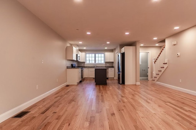 kitchen with backsplash, white cabinetry, light wood-type flooring, and appliances with stainless steel finishes