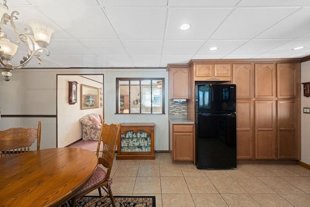 kitchen featuring black refrigerator, backsplash, a notable chandelier, and light tile patterned flooring