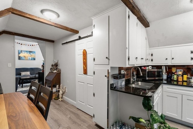 kitchen with light wood finished floors, decorative backsplash, a barn door, white cabinets, and a sink