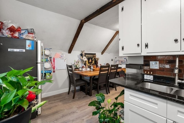 kitchen with white cabinets, lofted ceiling with beams, freestanding refrigerator, light wood-style floors, and a sink