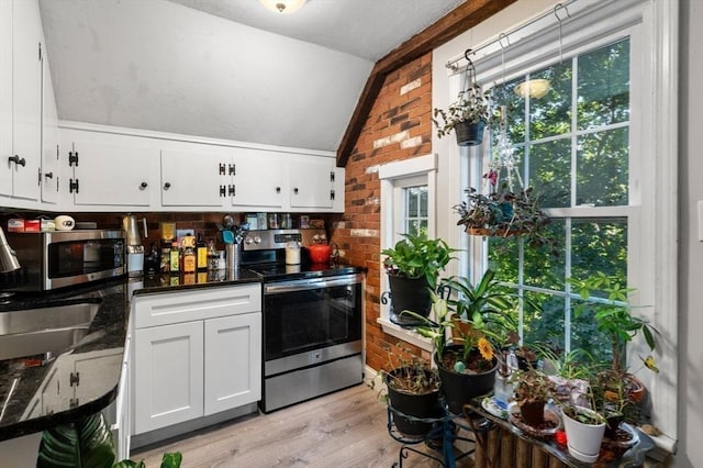 kitchen with light wood finished floors, lofted ceiling, dark countertops, appliances with stainless steel finishes, and white cabinetry