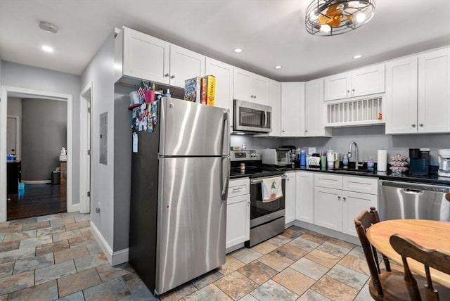 kitchen with appliances with stainless steel finishes, stone finish flooring, white cabinets, and a sink