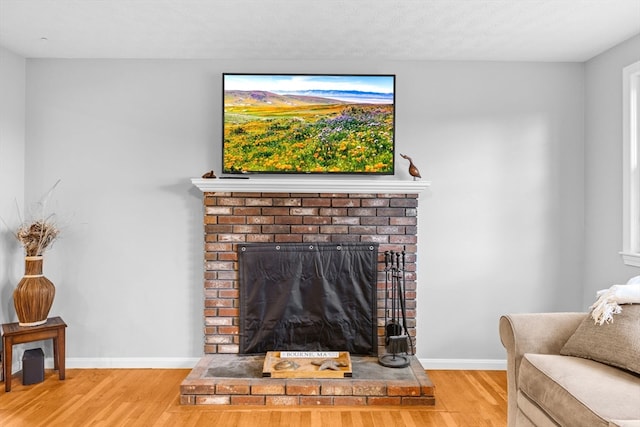 living room featuring wood-type flooring, a textured ceiling, and a brick fireplace