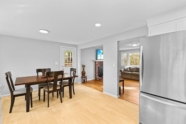 dining space featuring light wood-type flooring and a brick fireplace