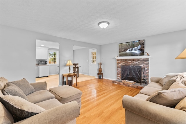 living room featuring a textured ceiling, light wood-type flooring, and a brick fireplace