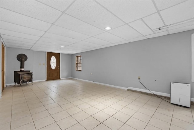 interior space featuring a wood stove, light tile patterned floors, a paneled ceiling, and baseboards