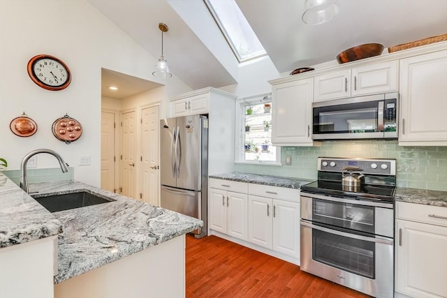 kitchen with lofted ceiling with skylight, appliances with stainless steel finishes, sink, white cabinets, and hanging light fixtures