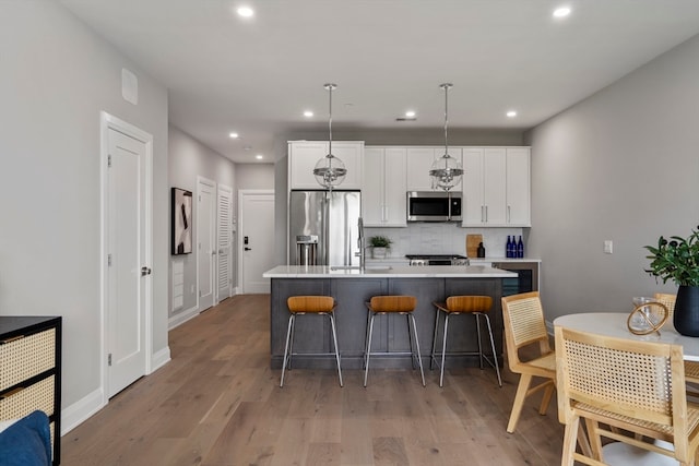 kitchen featuring pendant lighting, an island with sink, light hardwood / wood-style flooring, white cabinetry, and stainless steel appliances