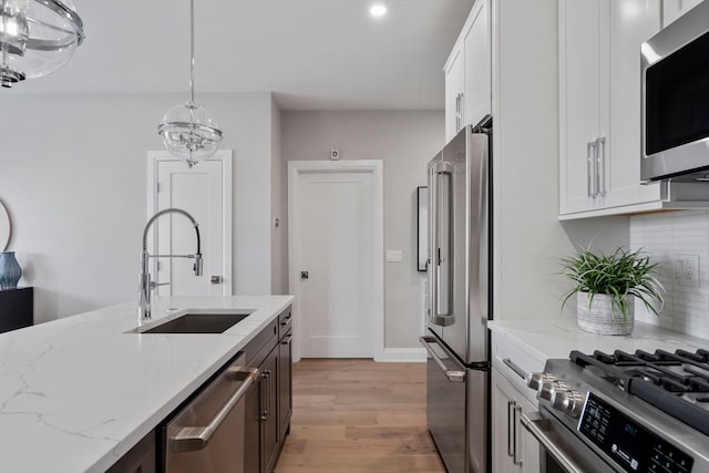 kitchen with sink, decorative light fixtures, white cabinetry, appliances with stainless steel finishes, and light stone countertops