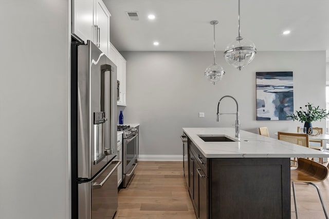 kitchen with appliances with stainless steel finishes, hanging light fixtures, white cabinets, light hardwood / wood-style flooring, and sink