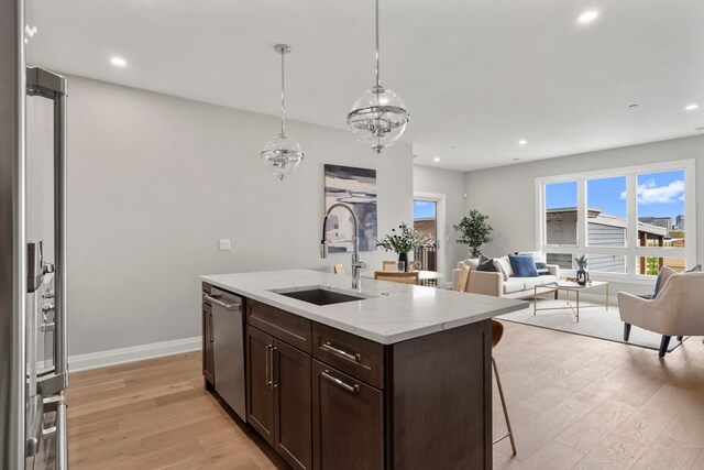 kitchen featuring an island with sink, dishwasher, light hardwood / wood-style flooring, decorative light fixtures, and sink