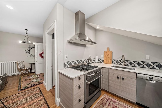 kitchen featuring radiator heating unit, appliances with stainless steel finishes, sink, light wood-type flooring, and island exhaust hood