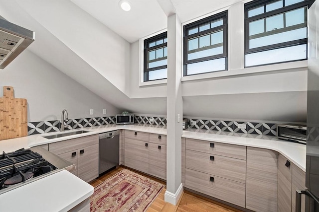 kitchen with light hardwood / wood-style flooring, dishwasher, sink, a towering ceiling, and wall chimney range hood