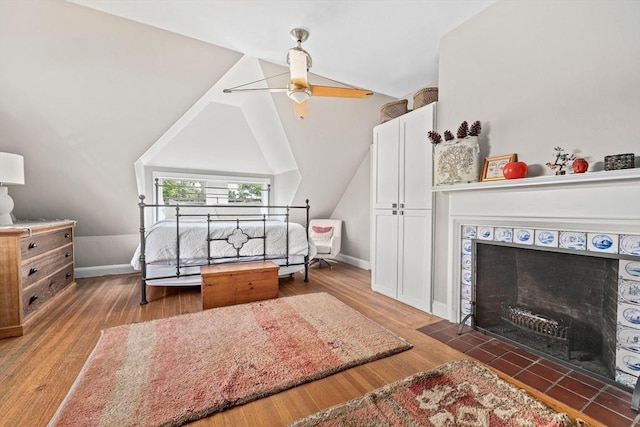 bedroom with ceiling fan, dark hardwood / wood-style floors, a tiled fireplace, and vaulted ceiling