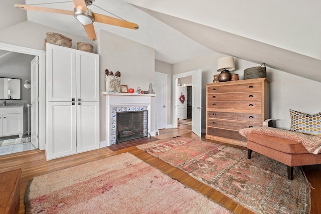 living room with ceiling fan, hardwood / wood-style floors, a tiled fireplace, and vaulted ceiling