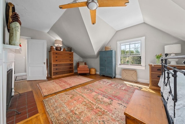 bedroom with hardwood / wood-style flooring, a brick fireplace, ceiling fan, and vaulted ceiling