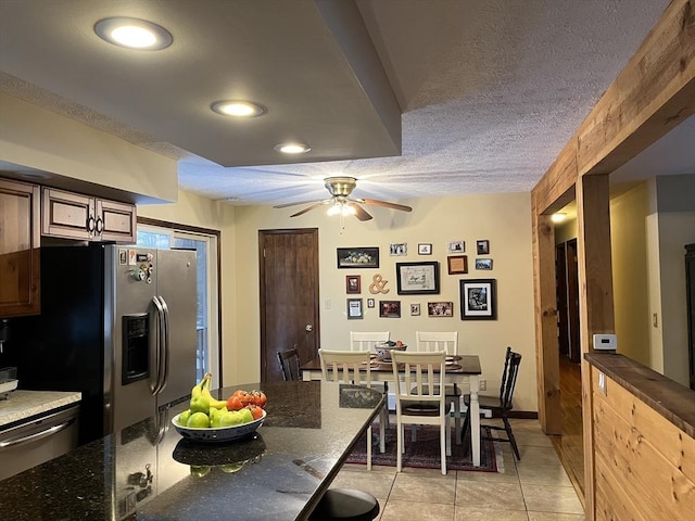 kitchen with appliances with stainless steel finishes, dark stone countertops, light tile patterned floors, ceiling fan, and a textured ceiling