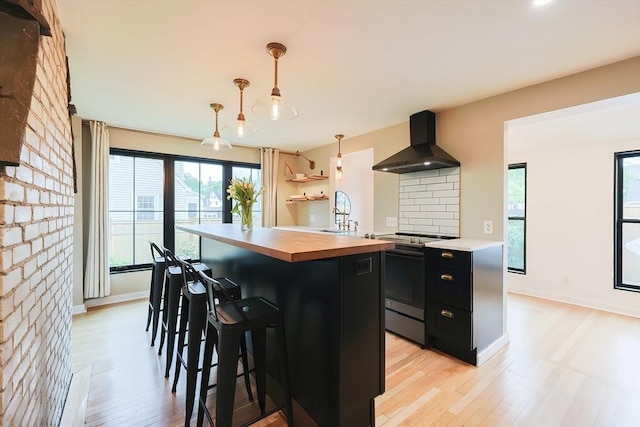 18 Carolina St, Medford, MA 02155 - kitchen featuring wall chimney range hood, butcher block counters, stainless steel stove, dark cabinetry, and healthy amount of natural light