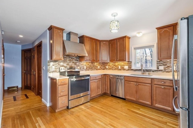 kitchen featuring sink, wall chimney range hood, pendant lighting, appliances with stainless steel finishes, and light wood-type flooring